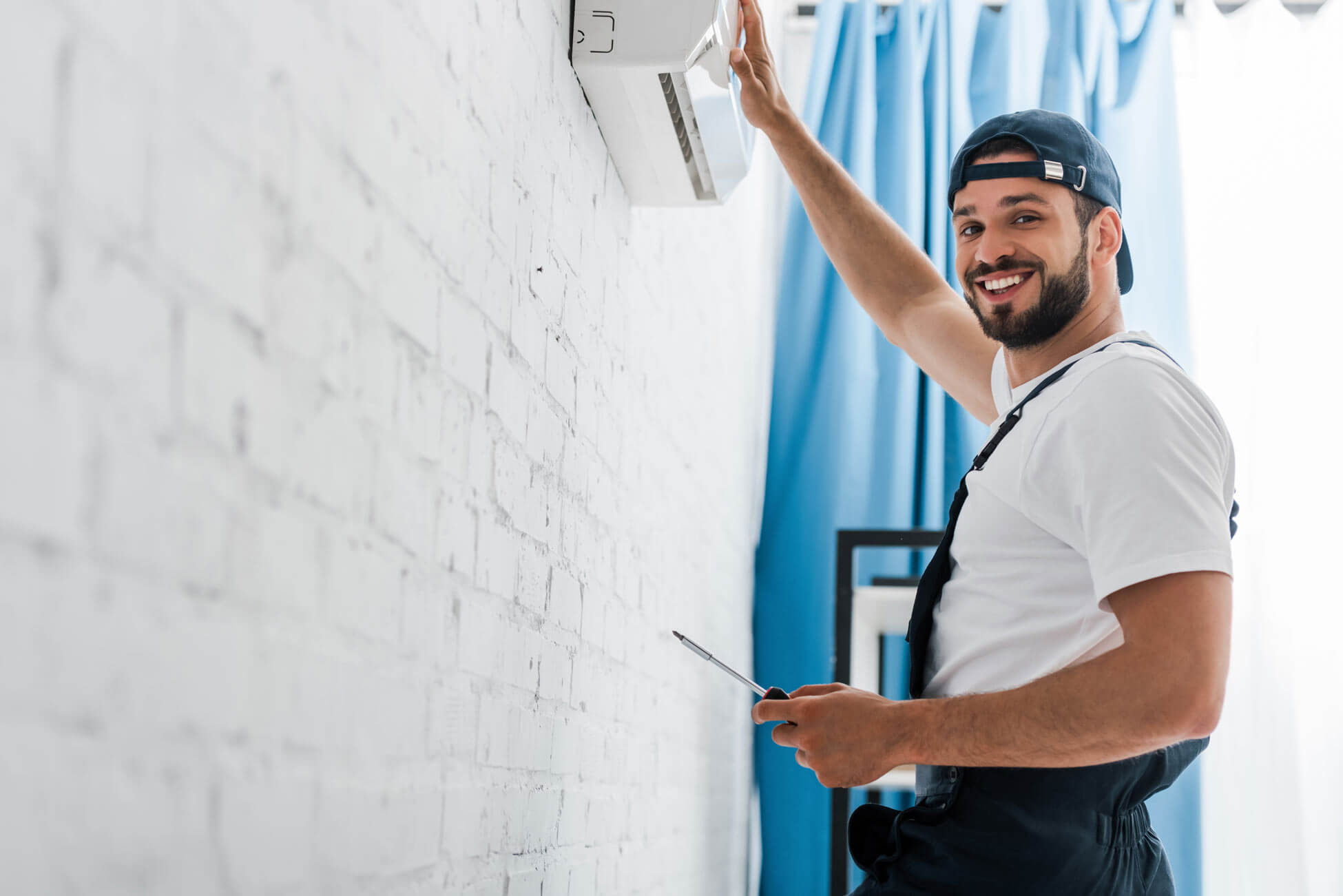 Smiling-workman-looking-at-camera-while-repairing-air-conditioner